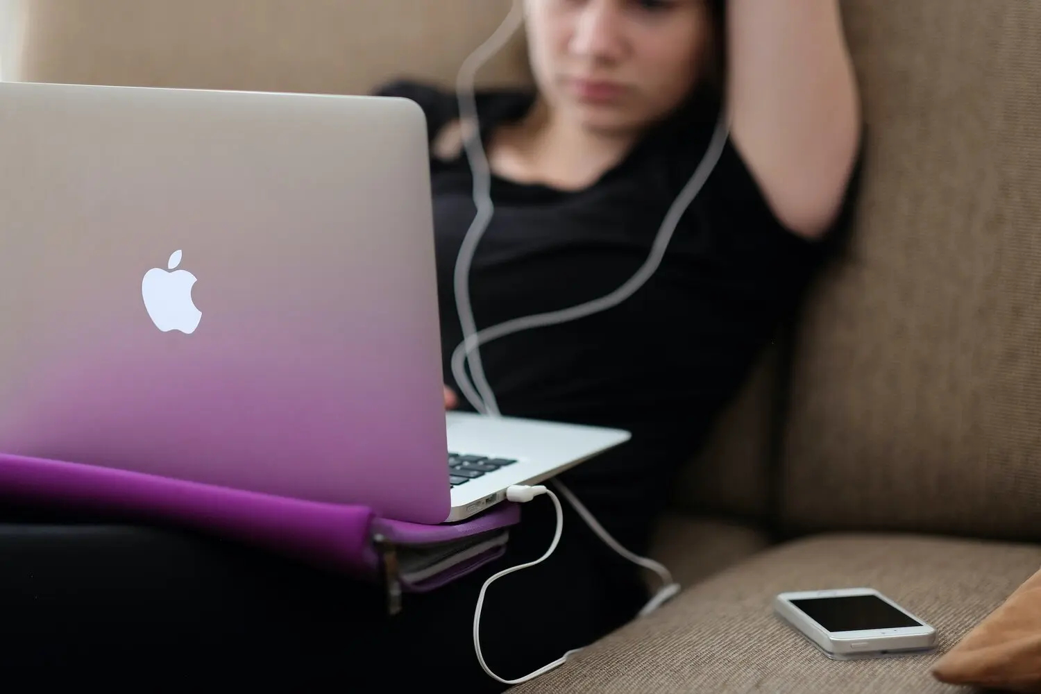Young woman sitting on a couch and working on a laptop with headphones in