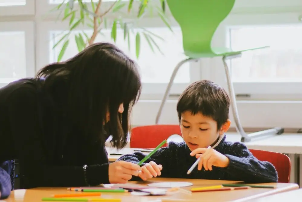 Child coloring and speaking with a teacher