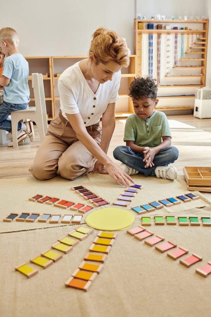 teacher and young boy playing with colorful wooden bricks on floor