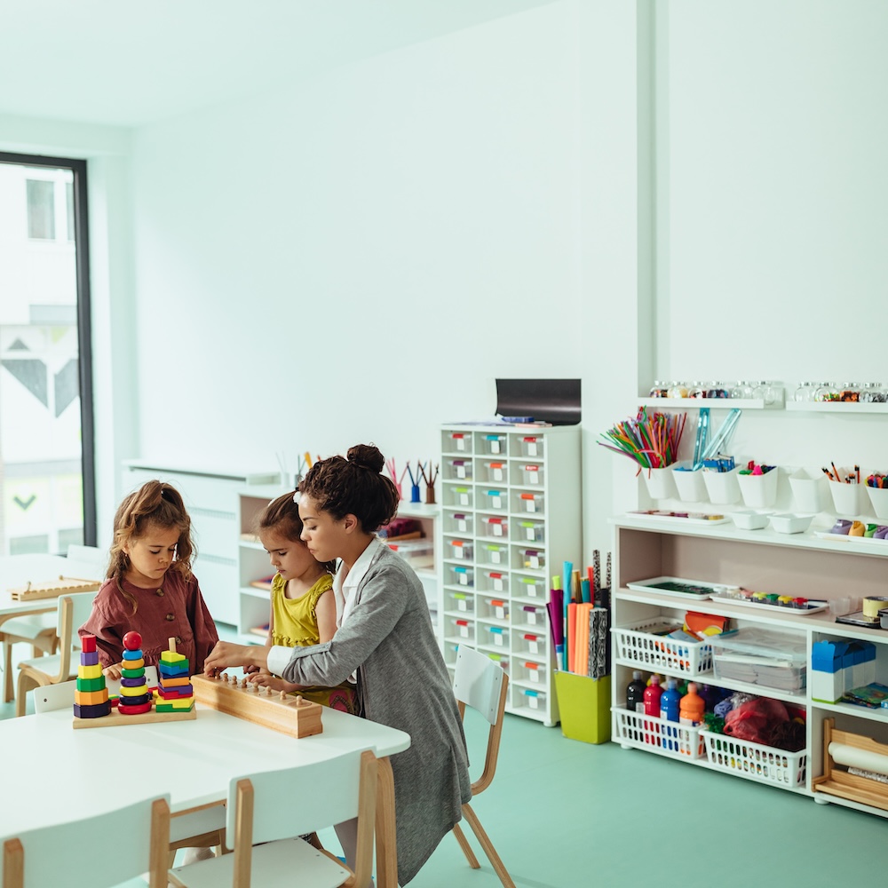 Mother sitting with daughters in classroom playing with blocks