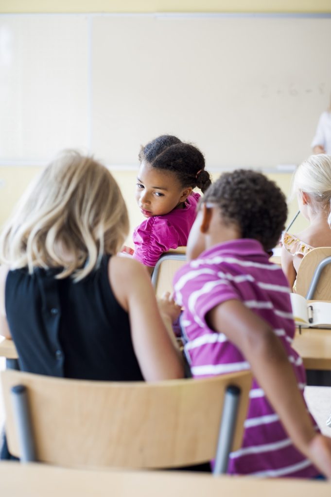 A young girl in a pink shirt attentively listening in class