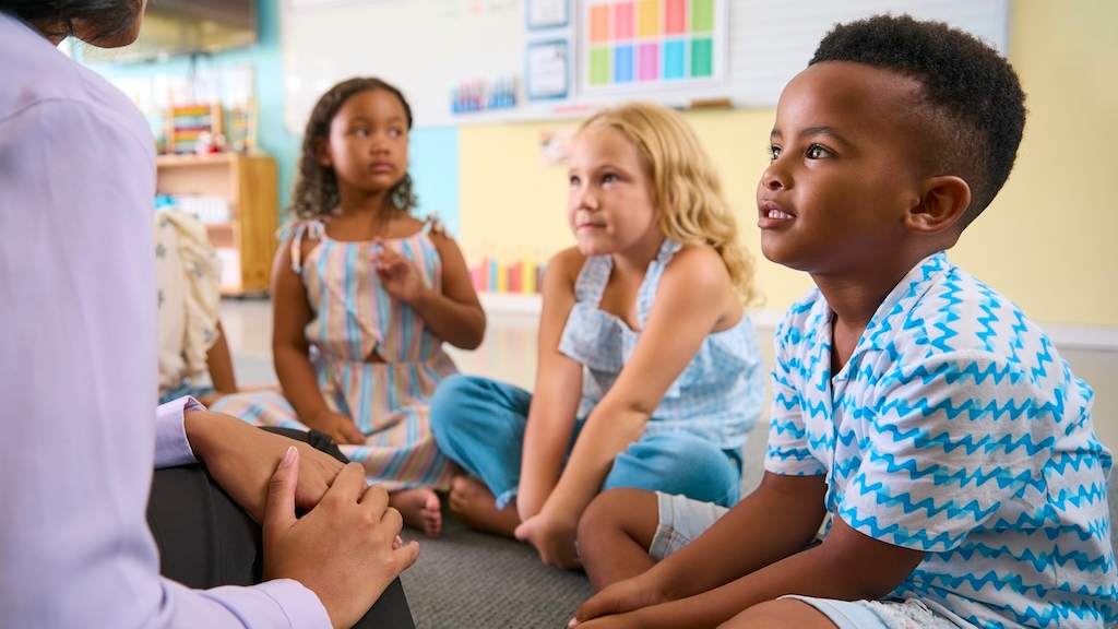 Elementary school teacher sitting with children in class performing different assessments. 