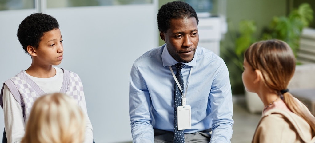 Portrait of young psychologist listening to children in support group circle