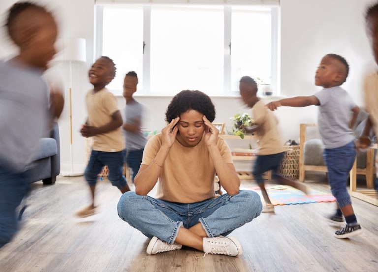 Shot of a young woman looking stressed out while her children run around her at home.