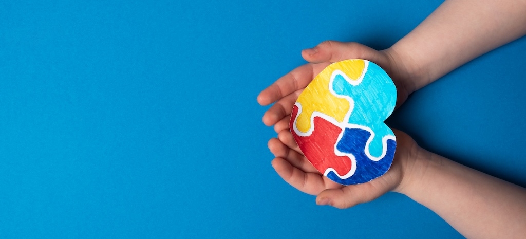 Autism awareness day concept. Child hands holding colorful puzzle heart on blue background