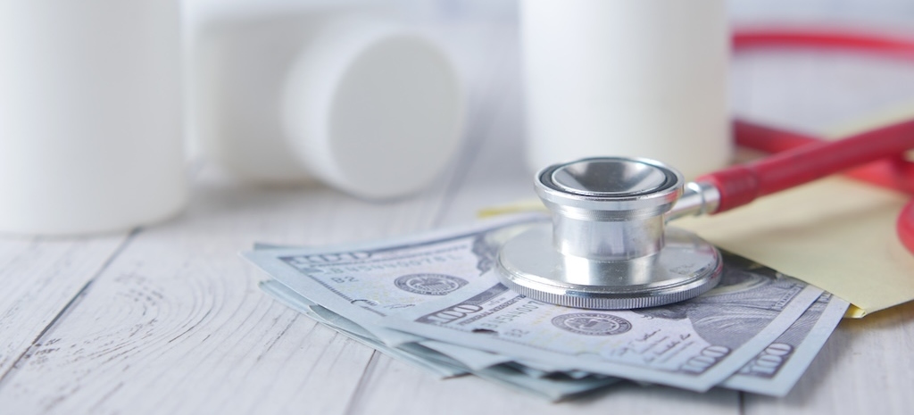 Healthcare cost concept with us dollar , container and pills on table .