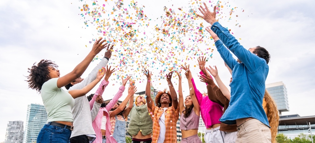 Happy playful group of young friends bonding outdoors, celebrating and throwing confetti