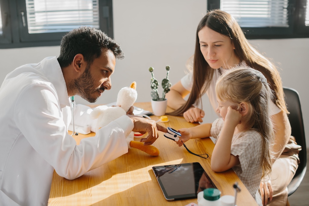 A young pediatrician comforting young child in autism testing clinic, taking pulse and vitals.