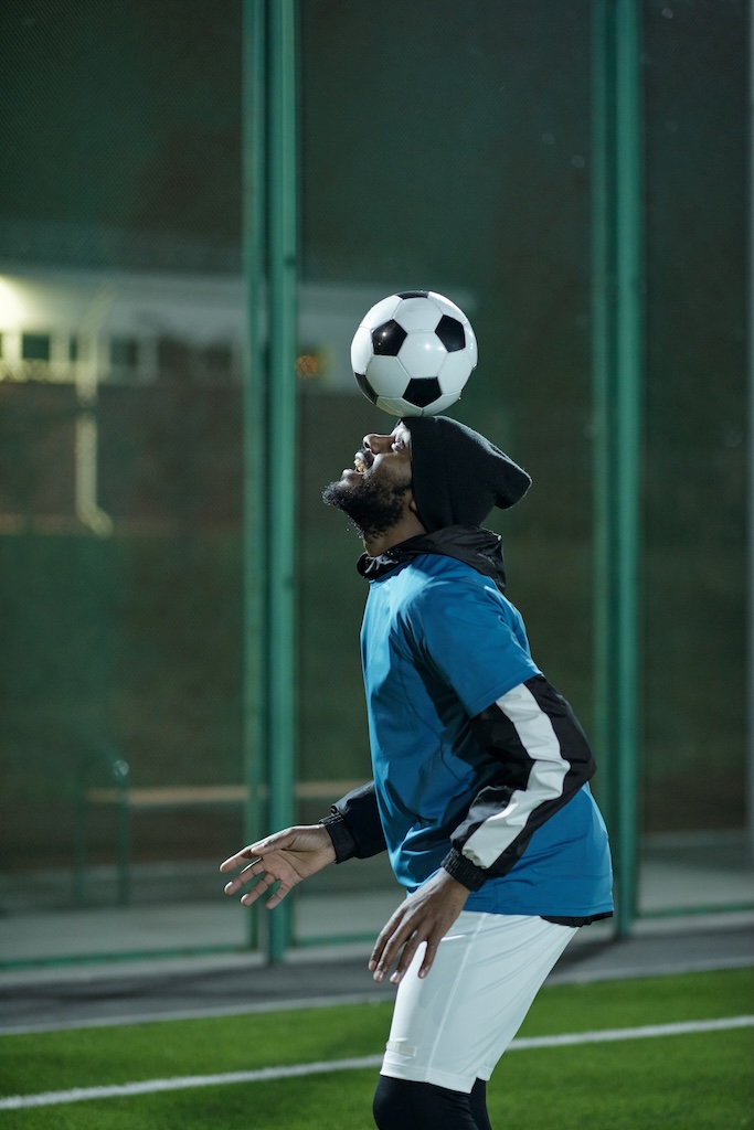 Young handsome man in sports uniform exercising with soccer ball on his forehead while training at stadium