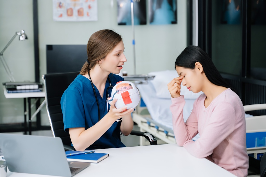 Female Doctor and patient discussing something while sitting at the table, patient holding their head in pain
