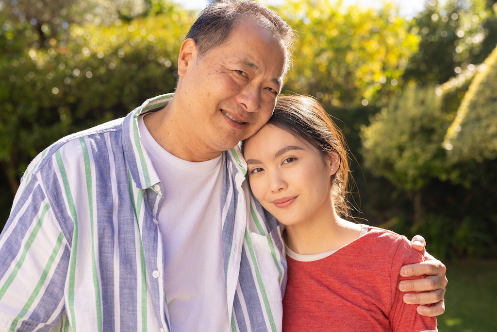 Young woman and her father, embracing and smiling outdoors