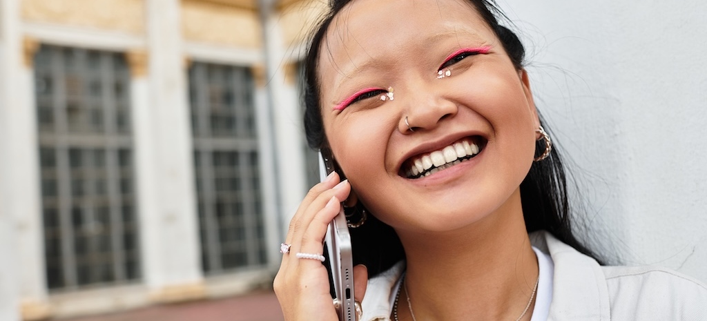 A stylish young woman smiles brightly while talking on her phone, 