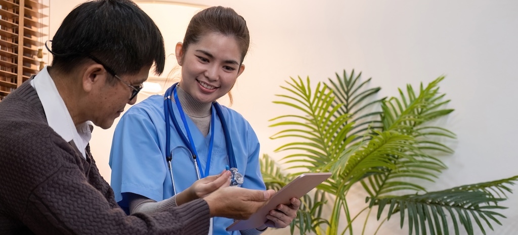 A cheerful caregiver in blue scrubs helps an elderly man with his paperwork,