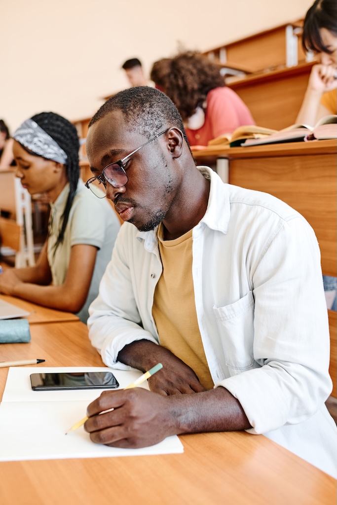 student in eyeglasses concentrating on writing exam at desk at auditorium of university