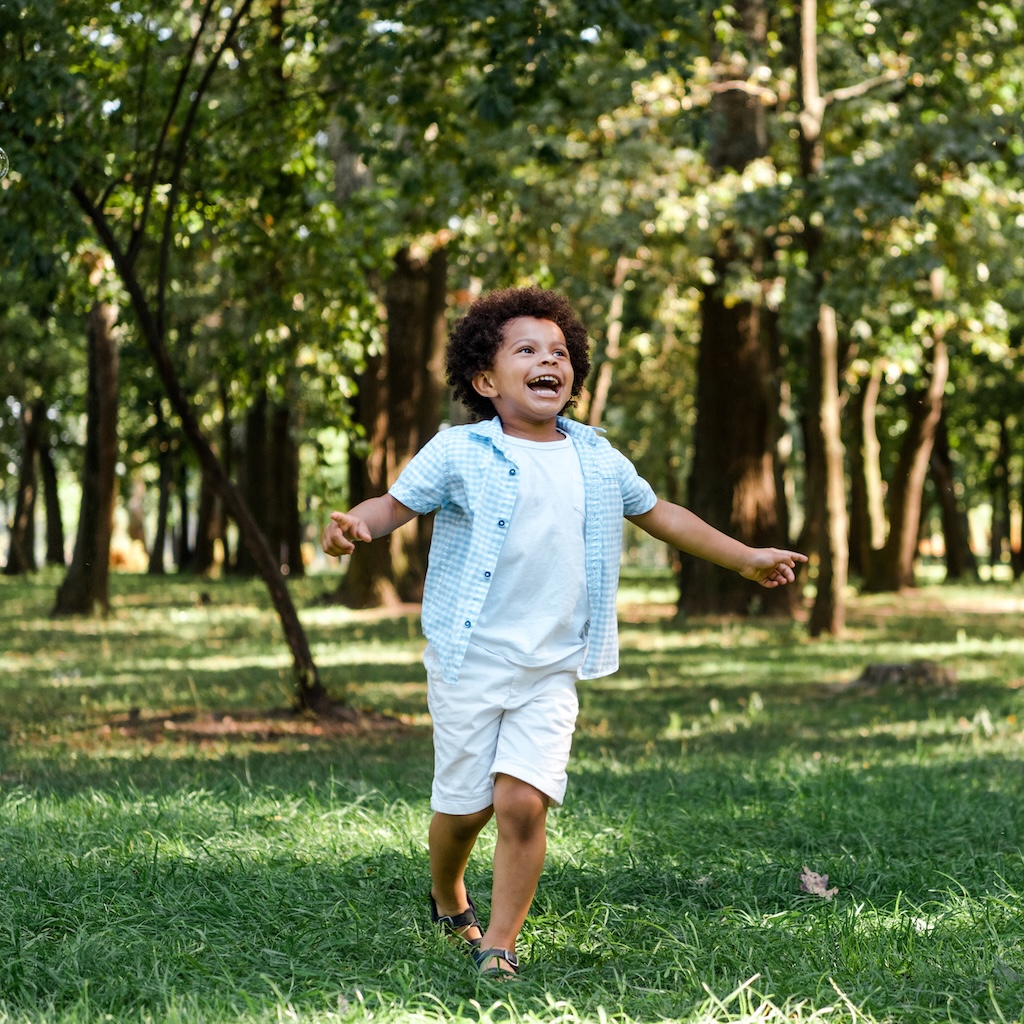 happy african american boy running on green grass in park