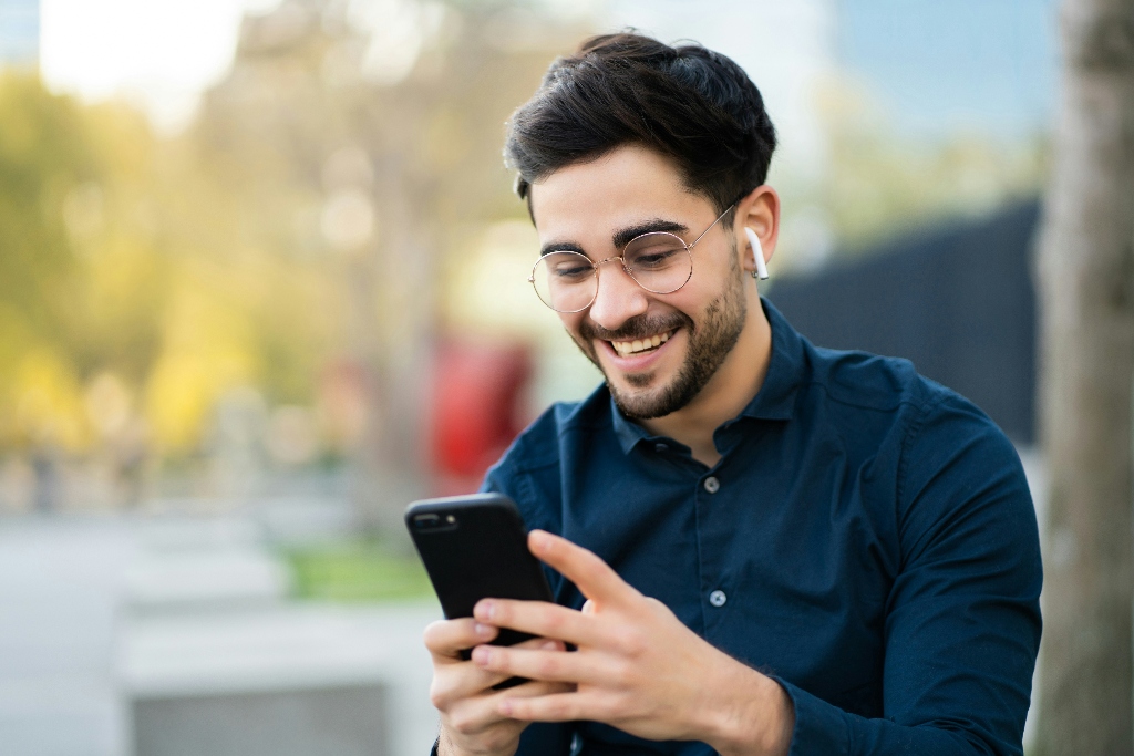Young gentleman on his phone, smiling with headphones in.