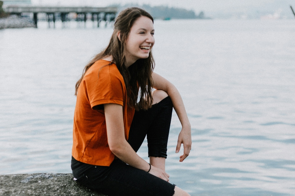 Young woman sitting on the edge of the dock, water hanging over into the water at the ocean