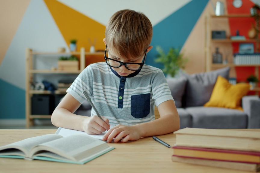 Young boy learning and writing on his assignment in school.