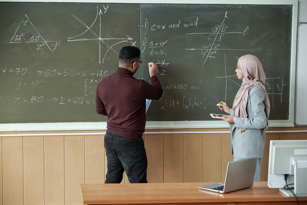 Adult working through math problems on a chalkboard with a clinician, representing challenges with numerical reasoning assessed in dyscalculia testing