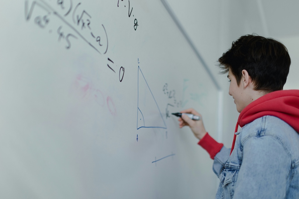 Teen working through a math problem on a whiteboard, representing challenges with numerical reasoning assessed in dyscalculia testing