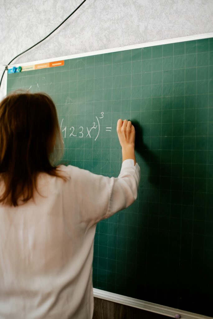 Student writing a math equation on a chalkboard, representing challenges with numerical processing assessed in dyscalculia testing
