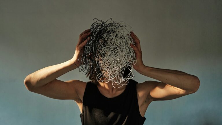 Person holding a tangled mass of black and white cords over their face with both hands, symbolizing feelings of mental overload and overwhelm.