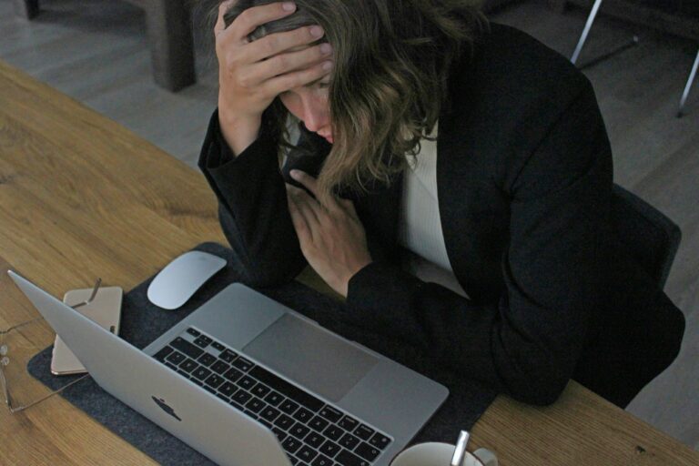 Person holding their head while sitting at a laptop, appearing mentally overwhelmed and emotionally exhausted.