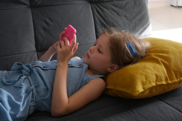 Young girl lying on a couch and looking at a smartphone, illustrating sensory issues in kids.