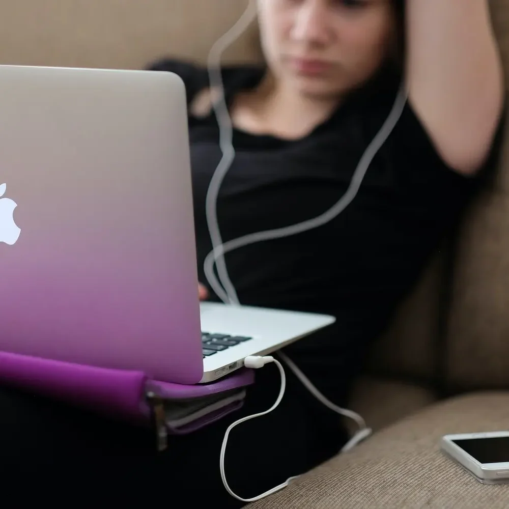 Young woman sitting on a couch and working on a laptop with headphones in