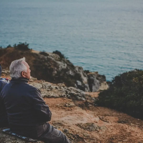 Two elderly people sitting on a bluff overlooking the ocean